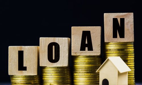 Saving money, home loan, mortgage, a property investment for future concept. A wooden block on stacked of coins with a small residence house on dark background. A sustainable investment.