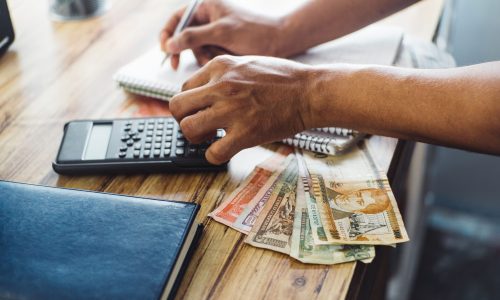 A selective focus of male hands writing and at the same time calculating Honduran lempiras