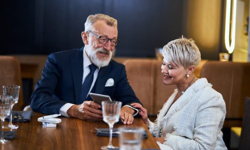 Beautiful senior couple spending time together in rich restaurant look at gadget, smile, cheerful