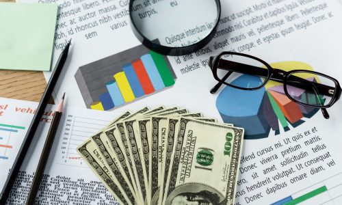 top view of magnifier and glasses on charts near dollar banknotes on desk